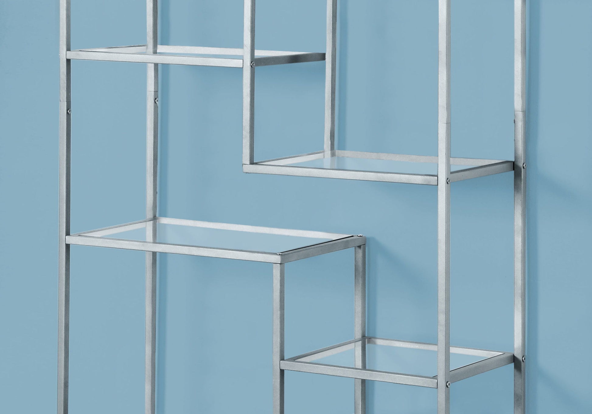 A contemporary metal bookshelf with glass shelves, arranged in a staggered design, is set against a light blue wall. Ideal as an office bookcase or modern etagere.
