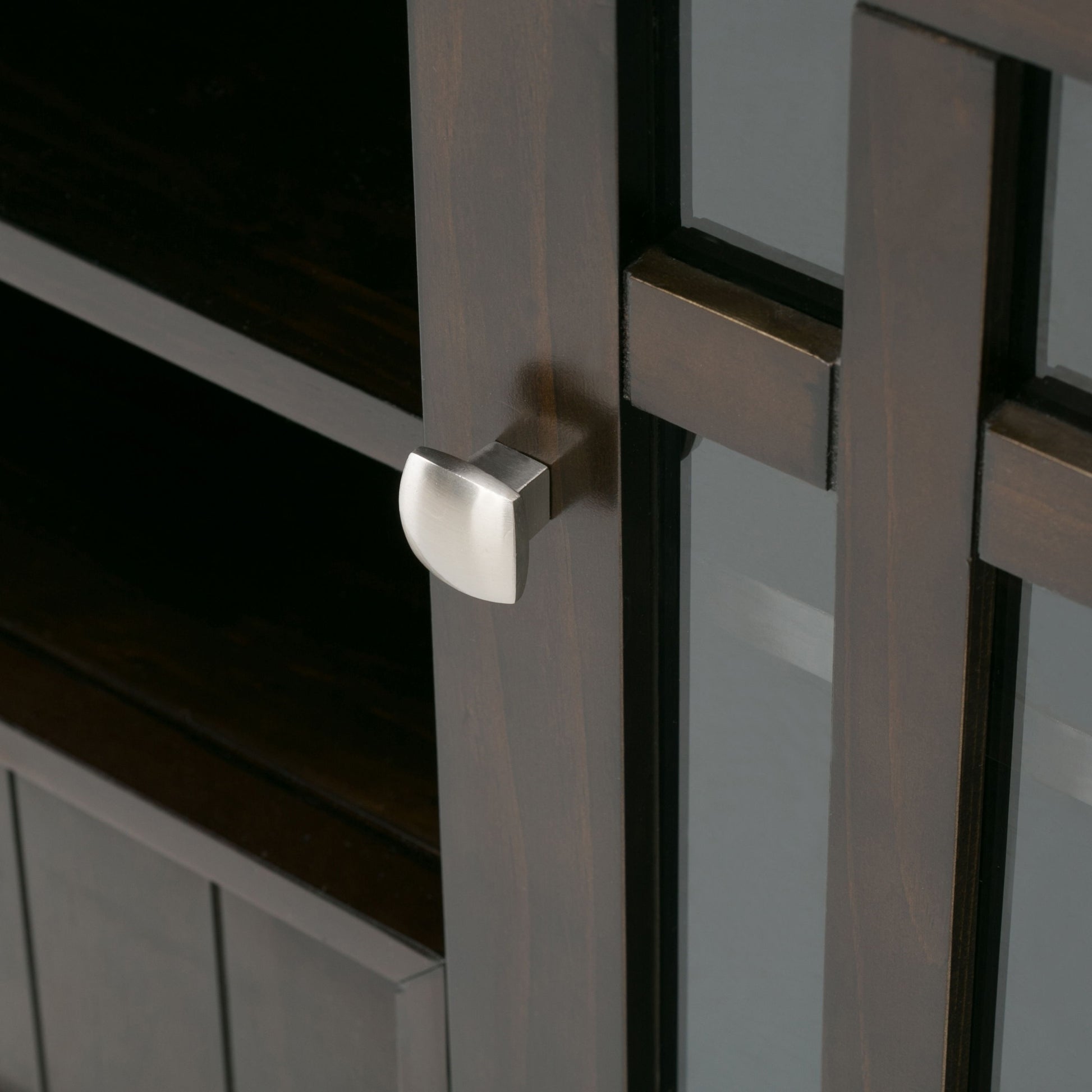 Close-up of the Bedford Handcrafted Tall TV Media Stand, showing a dark wooden cabinet with a glass panel door and modern square silver knob. Interior shelves are visible through the glass.
