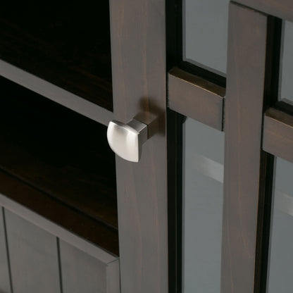 Close-up of the Bedford Handcrafted Tall TV Media Stand, showing a dark wooden cabinet with a glass panel door and modern square silver knob. Interior shelves are visible through the glass.