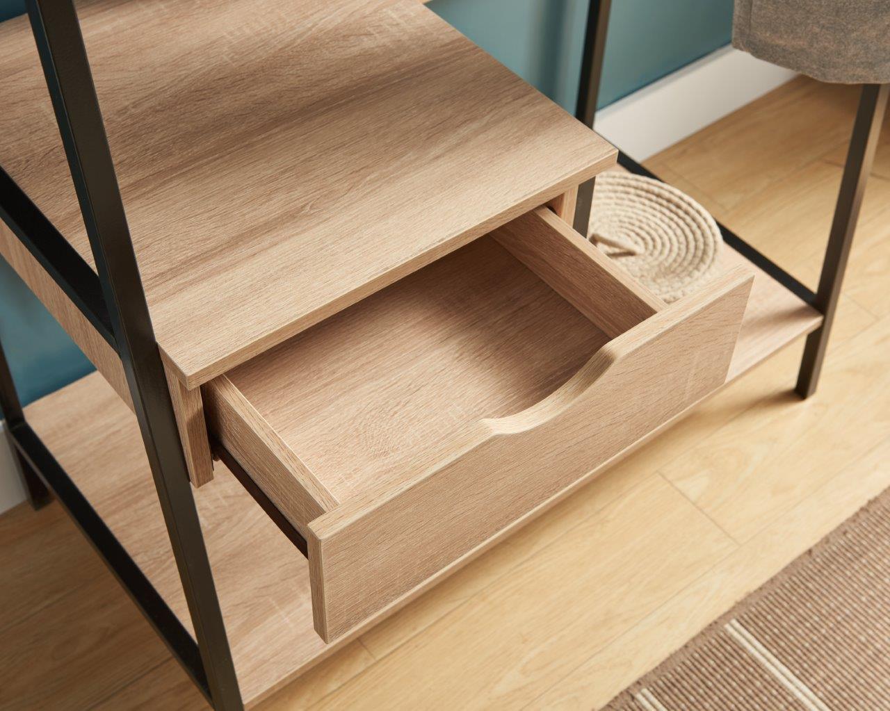 A close-up of the Metal Clothes Rack Open Wardrobe shows its black metal frame and wooden drawer pulled open. The free-standing unit sits on a light wood floor beside a woven rug and coiled rope basket, featuring a hanging clothes rod.