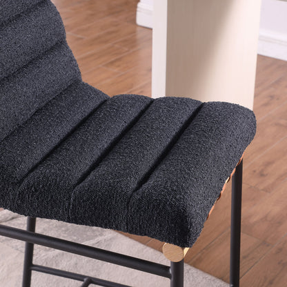 Close-up of the Lahni - 17" Boucle Fabric Counter Height Chair, featuring a textured dark gray seat and black metal legs, placed on a wooden floor beside a light-colored table.