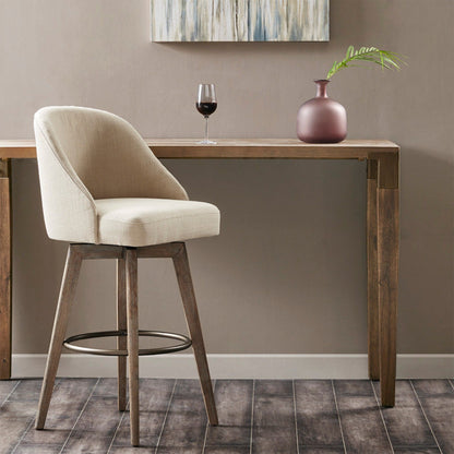 A sand-colored bar stool with a swivel seat sits by a wooden table holding a glass of red wine, a pink vase with a green leaf, and is set against the backdrop of a modern abstract painting on the wall.