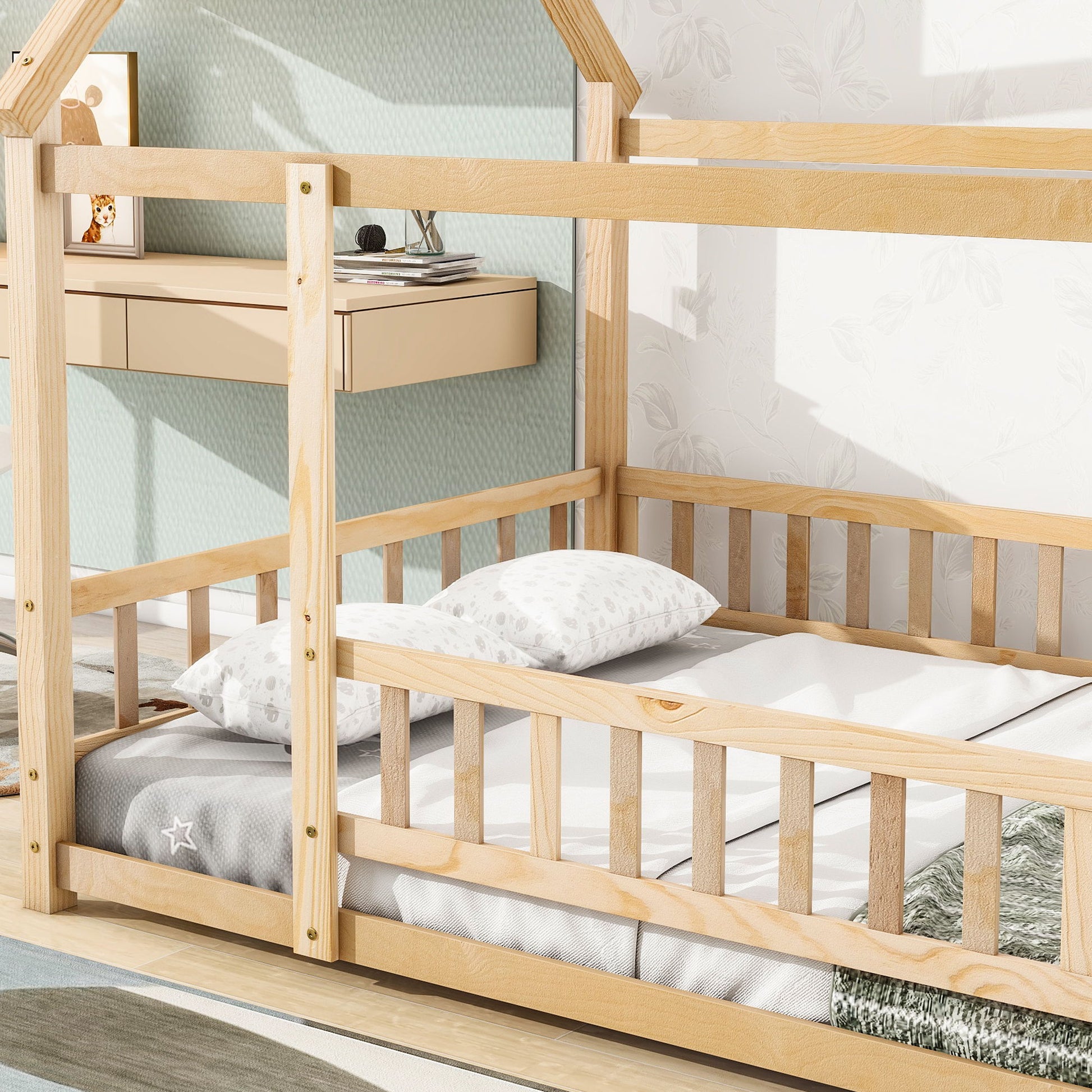 The Floor Wooden Bed With House Roof Frame and Fence Guardrails sits on a light wood floor, dressed in white and grey star bedding, next to a wall with light wallpaper and a floating beige drawer.