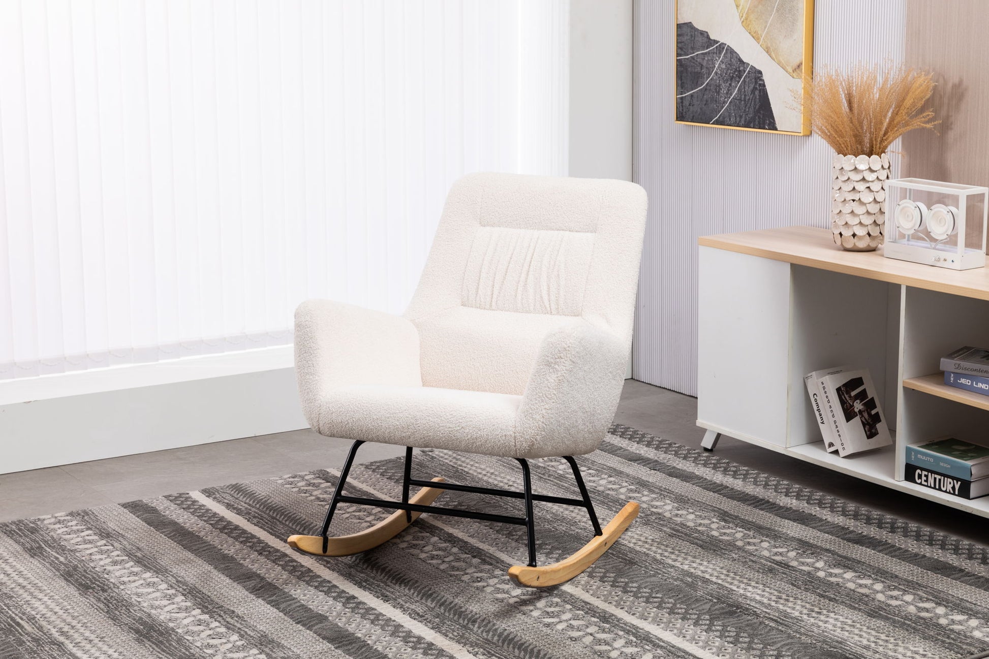 The Rocking Chair Nursery, Teddy Upholstered Glider Rocker in cream with wood rockers and black metal legs sits on a patterned gray rug in a bright, minimalist living room with white walls.