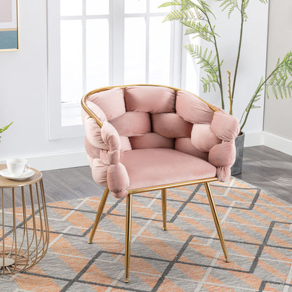 The Luxury Modern Simple Leisure Velvet Single Sofa Chair with pink tufted cushions and gold metal legs is placed on a patterned rug in a bright room with large windows, green plants, and a nearby small round table holding a teacup.