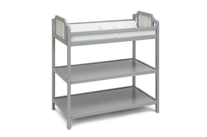 The Brees - Changing Table features a gray wooden design with decorative side paneling, two open shelves for storage, and a white cushioned changing pad on top.