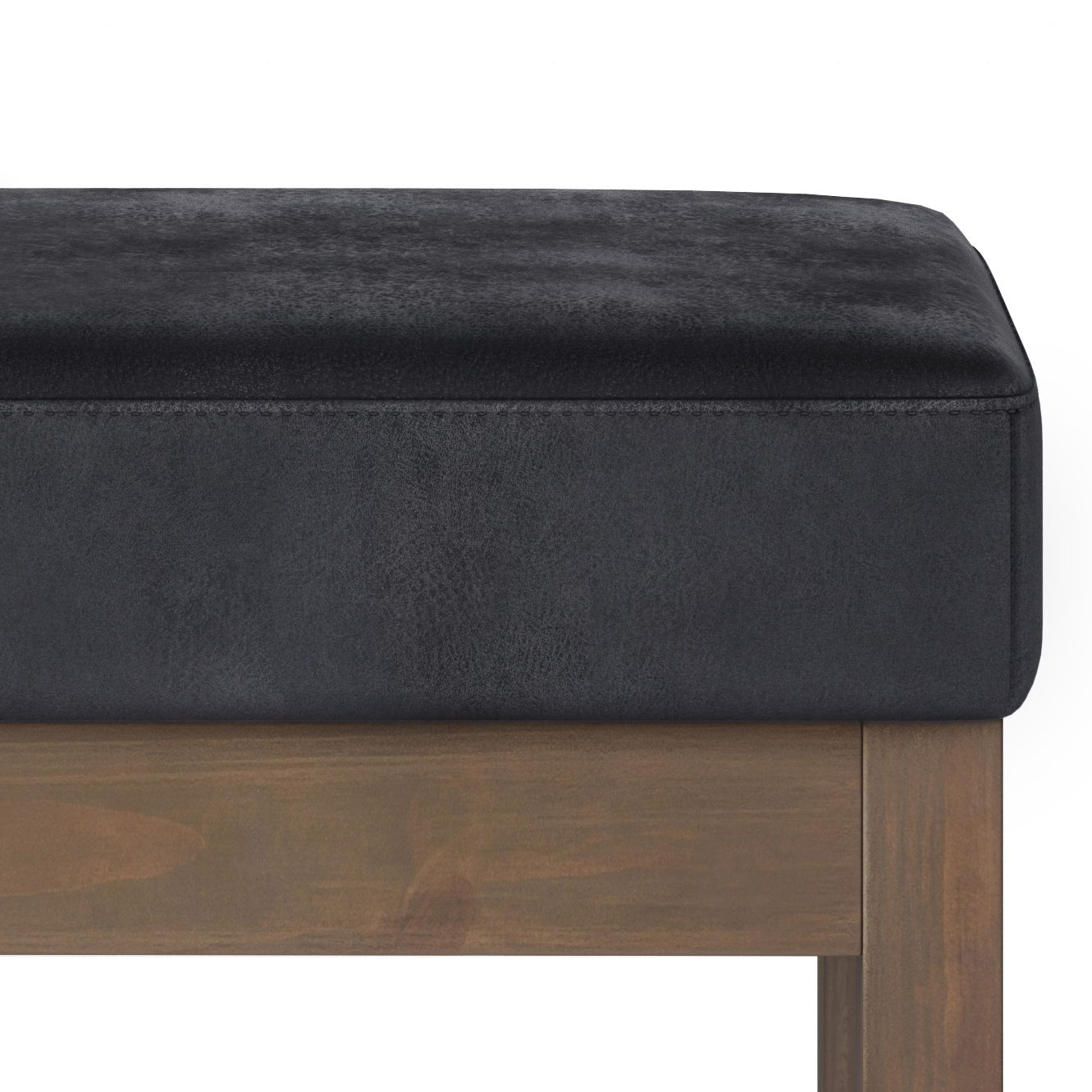Close-up of Milltown - Upholstered Ottoman Bench, featuring a black cushioned seat and wooden leg against a white background. Only the top part of the bench and one leg are shown.