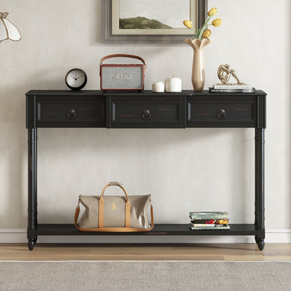 The Console Table Sofa Table With Drawers For Entryway features three drawers holding a vintage radio, a vase with yellow tulips, and books. On the long lower shelf are a beige duffel bag and stacked magazines, with framed artwork displayed above.