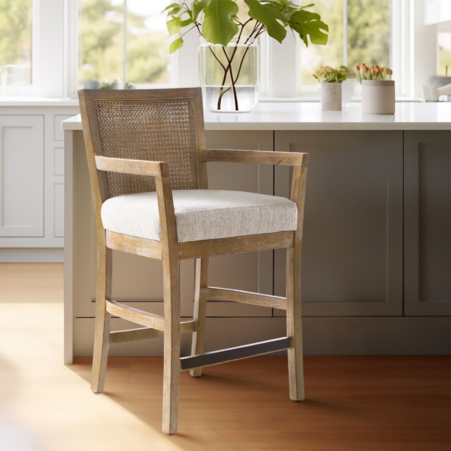 The Cane Back Counter Stool With Upholstered Seat - Cream / Reclaimed Natural sits by a kitchen island with gray cabinets, while green plants and sunlight can be seen in the background.
