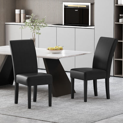 A set of two Contemporary Dining Chairs With Rubberwood Legs in black sits by a light rectangular dining table topped with fruit and a plant. The room features a gray rug, minimalist cabinets, and a built-in oven in the background.