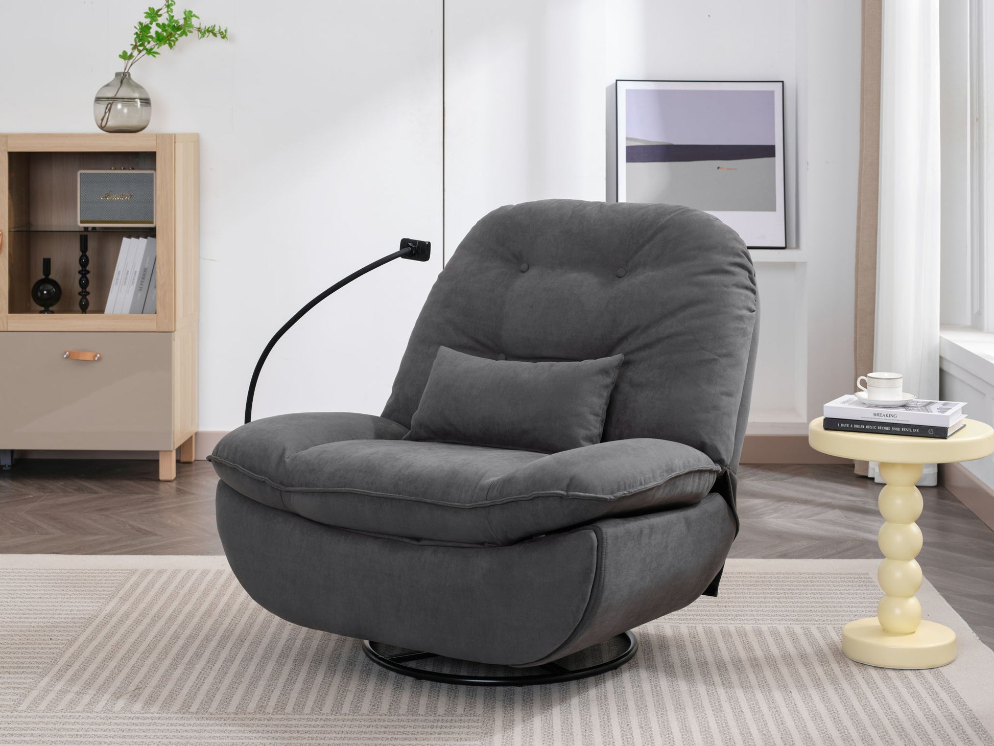 A modern living room with a Power Recliner Swivel Glider featuring a built-in reading light, USB charger, Bluetooth music player, plush gray upholstery, small pillow, yellow round side table with books, bookshelf, plant, and wall art.