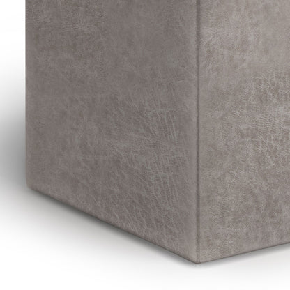Close-up of the corner of the Rockwood - Upholstered Cube Storage Ottoman With Tray, showing its grey, rectangular form and soft, textured upholstered surface against a white background.
