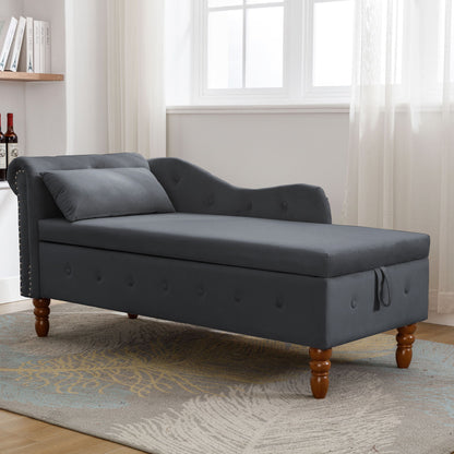 A gray Chaise Lounge Indoor features velvet upholstery, rolled arms, storage, a matching pillow, and nailhead trim. Perfect for living rooms, bedrooms, or offices, it's shown on a patterned rug in a bright room with large windows and sheer curtains.