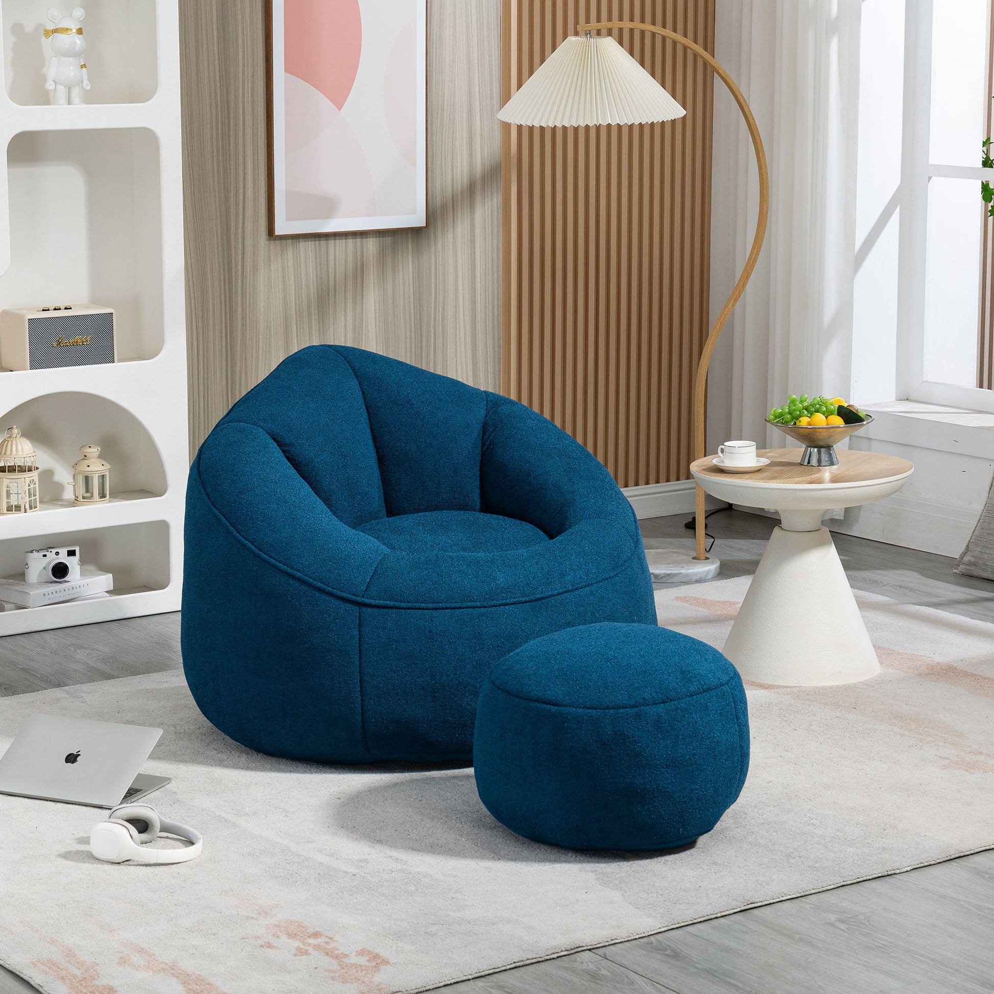 A modern living room featuring the Bedding Bean Bag Sofa Chair High Pressure Foam With Footrest on a light rug, a round side table with fruit and a teacup, plus a laptop and headphones on the floor in soft natural light.