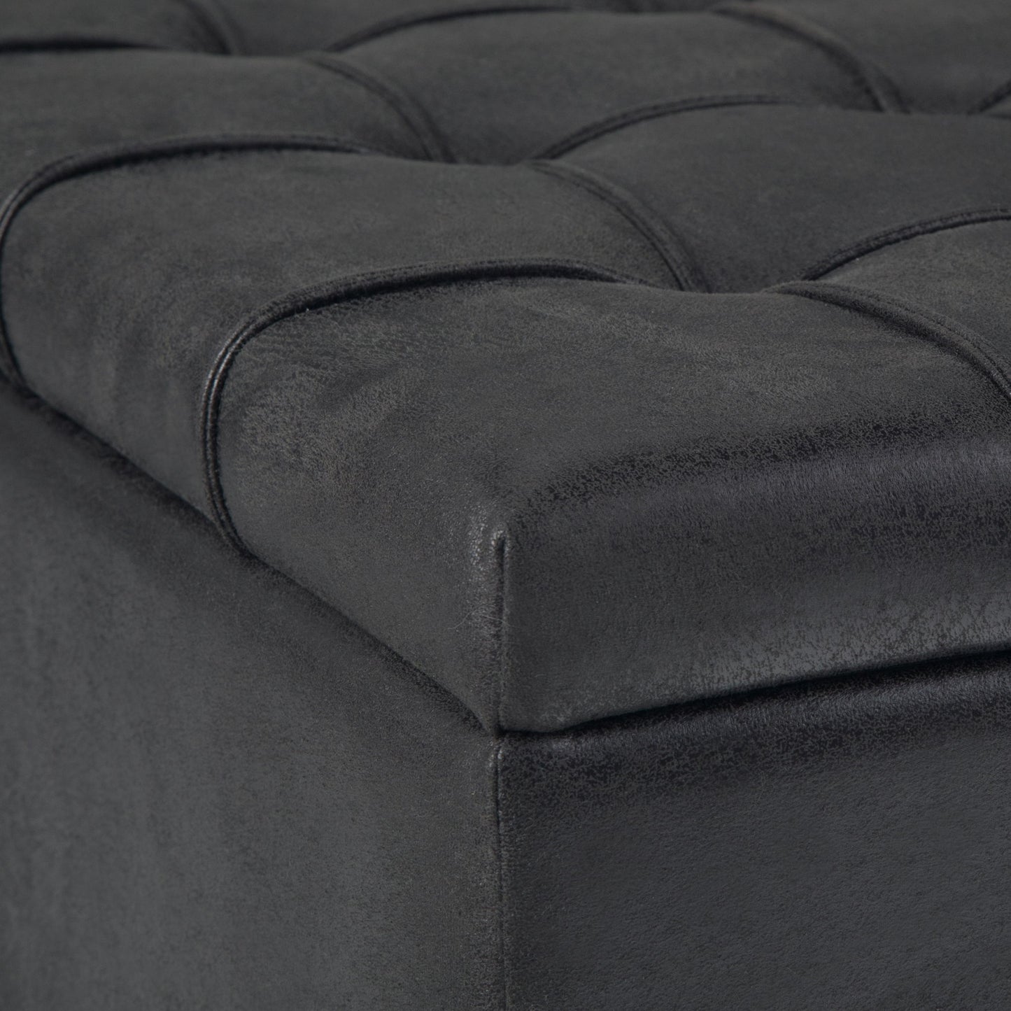 Close-up of the Harrison Upholstered Coffee Table Storage Ottoman in black, featuring a tufted faux leather surface with stitched square patterns on the cushioned top corner.