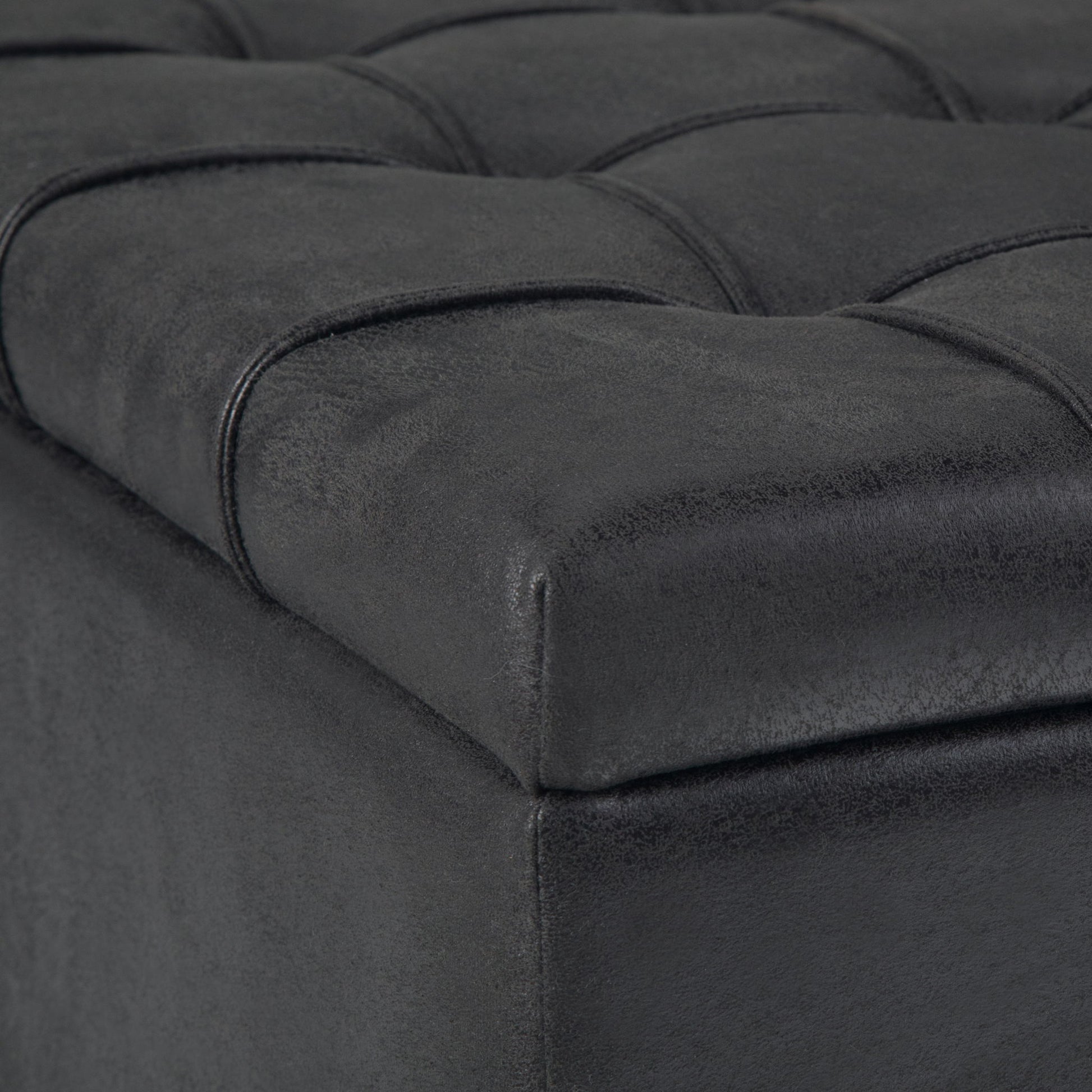Close-up of the Harrison Upholstered Coffee Table Storage Ottoman in black, featuring a tufted faux leather surface with stitched square patterns on the cushioned top corner.