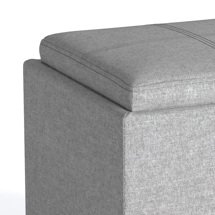Close-up of the top corner of the Rockwood Upholstered Cube Storage Ottoman With Tray in light gray, highlighting the cushioned lid, textured fabric, and stitching details.