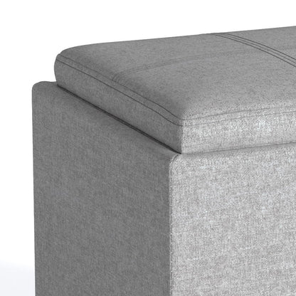 Close-up of the top corner of the Rockwood Upholstered Cube Storage Ottoman With Tray in light gray, highlighting the cushioned lid, textured fabric, and stitching details.