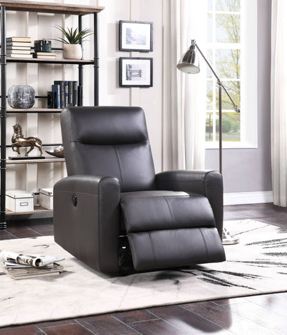 The Blane Top Grain Leather Match Power Motion Recliner in brown is set in a bright living room with a white rug, dark wood floors, bookshelves, framed wall art, a floor lamp, and large windows with white curtains.