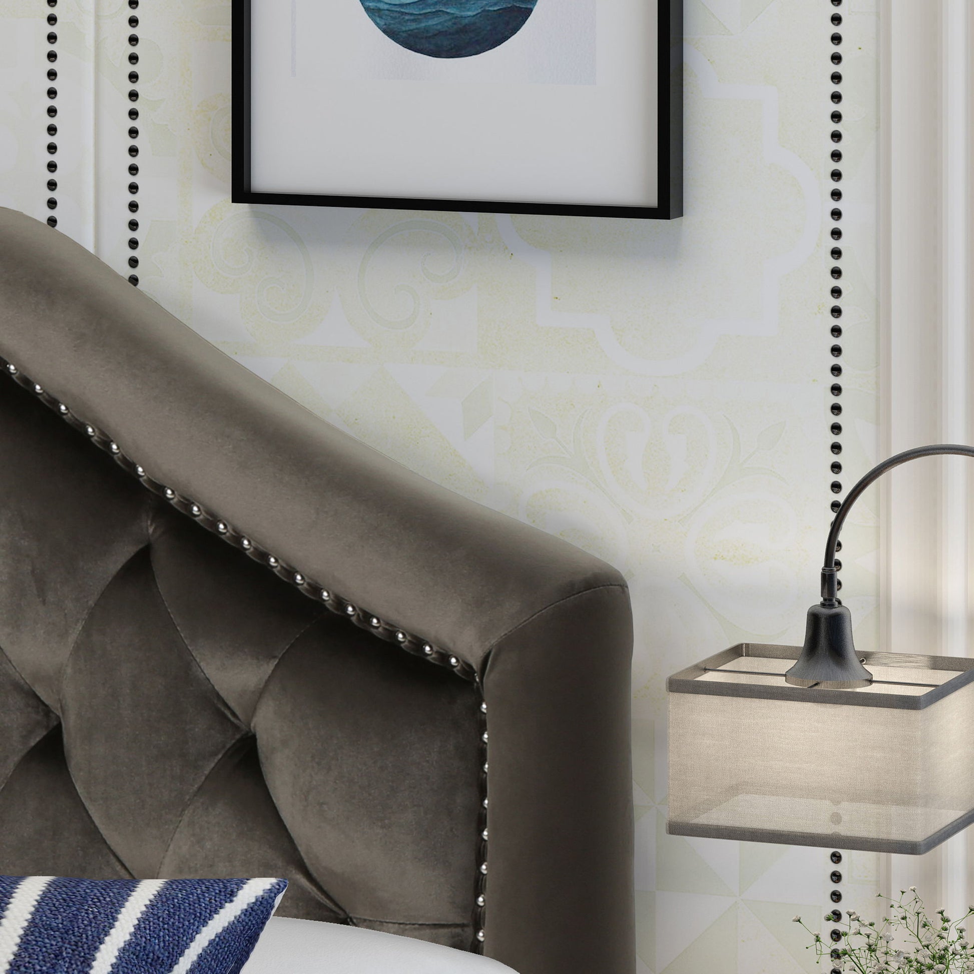 The Kaarina Contemporary Tufted Fabric Headboard in dark gray is paired with a wall-mounted lamp with a rectangular beige shade, a blue and white striped pillow, and framed abstract art on a light-patterned wall.