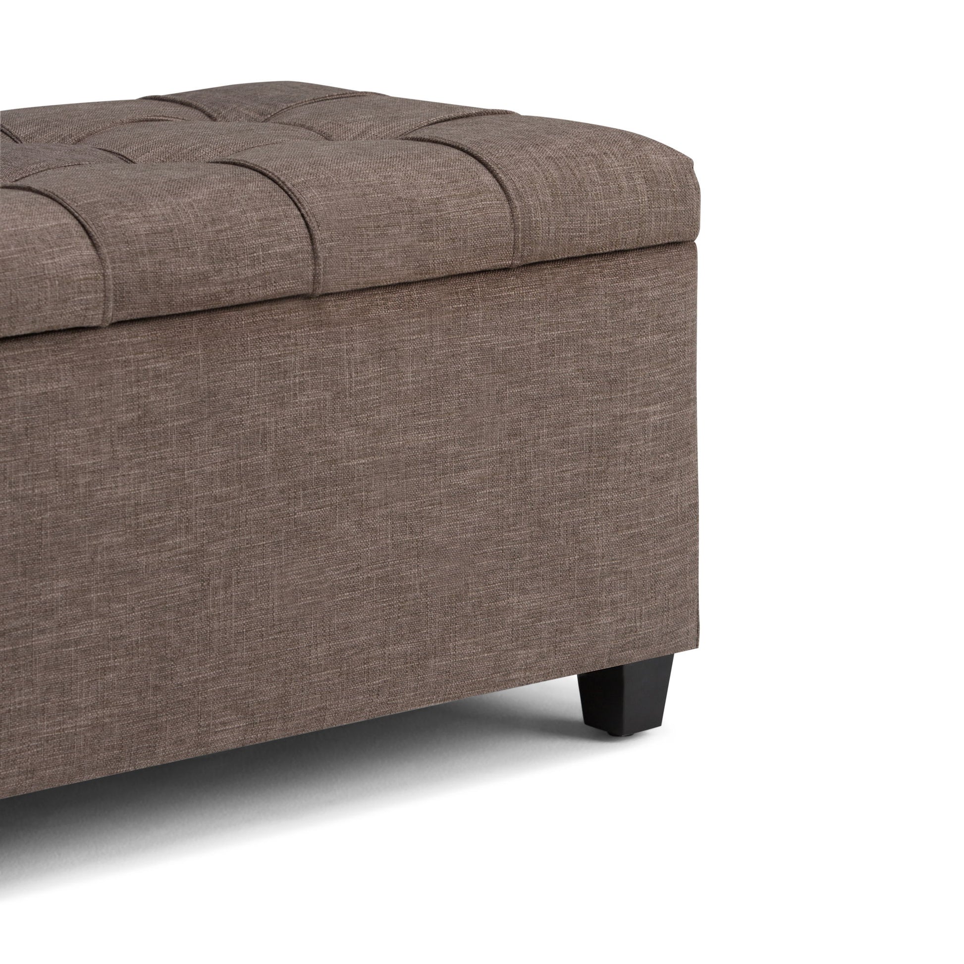 A close-up of the Sienna Upholstered Storage Ottoman Bench featuring brown fabric, a tufted cushioned lid, and short black legs, shown against a white background.