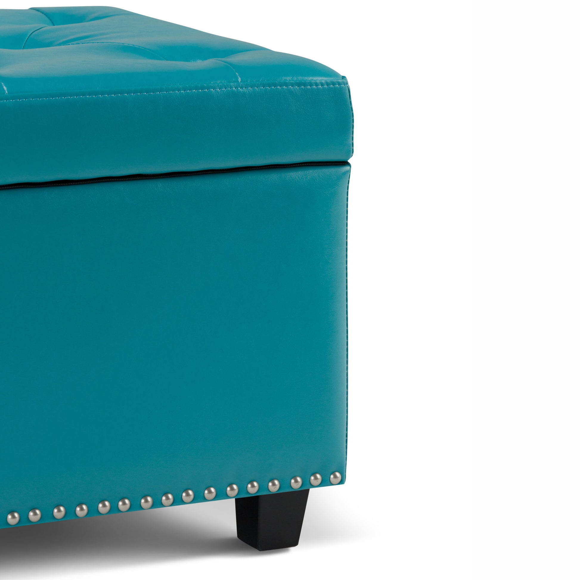 Close-up of the Hamilton - Upholstered Storage Ottoman in teal, featuring silver nailhead trim, black wooden legs, and visible stitching on the cushioned top.