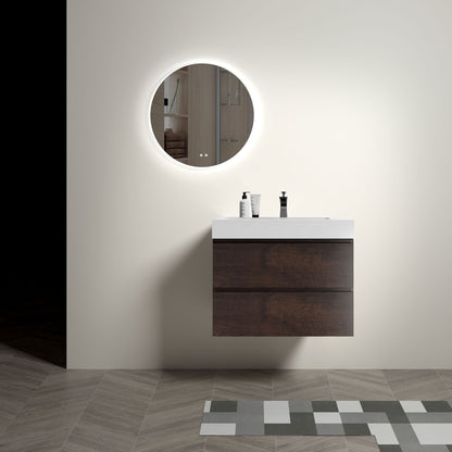 A minimalist bathroom features the Alice wall-mounted floating vanity with a one-piece sink basin, dark wood drawers, and a backlit round mirror. The white countertop holds two containers and geometric tiles cover the floor.