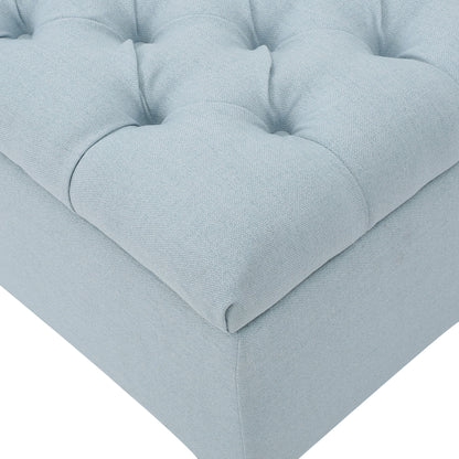 The Glouster Contemporary Storage Ottoman features a light blue, button-tufted upholstered cushion with soft, textured fabric, shown here on the corner of its square frame.
