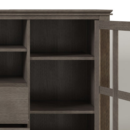 A close-up of the Artisan - Handcrafted, Tall TV Media Stand shows open shelves and a glass door on the right. Inside are two spacious shelves, with smaller shelves and drawers partially visible on the left.