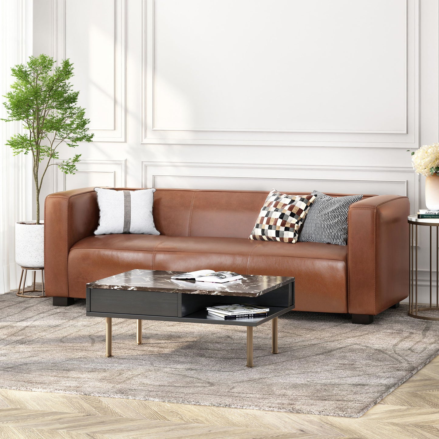 A modern living room featuring the Contemporary 3 Seater Sofa With Tuxedo Design in brown leather, two patterned cushions, a black marble coffee table, a potted plant, and a light rug on wooden floors with white paneled walls in the background.