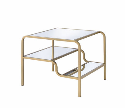 The Astrid - Mirrored Table features a gold metal frame and three clear glass shelves at varying heights, with the middle shelf showcasing a unique curved edge design.