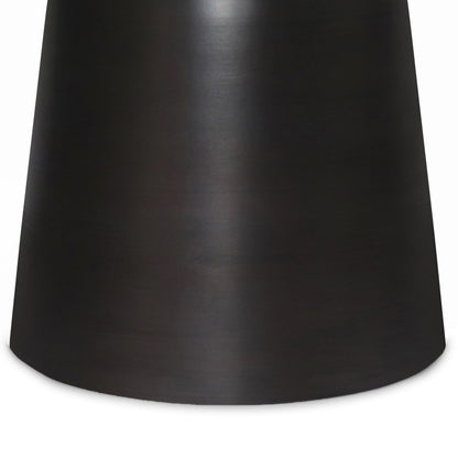 A close-up view of the lower part of the Toby - Handcrafted Metal Accent Table, featuring a dark, smooth, cylindrical surface with a slightly reflective metallic finish.