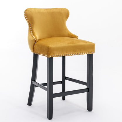 A set of 2 contemporary yellow velvet wing-back barstools with button tufting, chrome nailhead trim, and black wooden legs with footrests, shown against a plain white background.