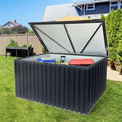 The Metal Storage Box Store Large Out Door Use - Black sits on a green lawn near a house and garden, its lid open to reveal storage for items such as a shovel, red container, and blue bucket.