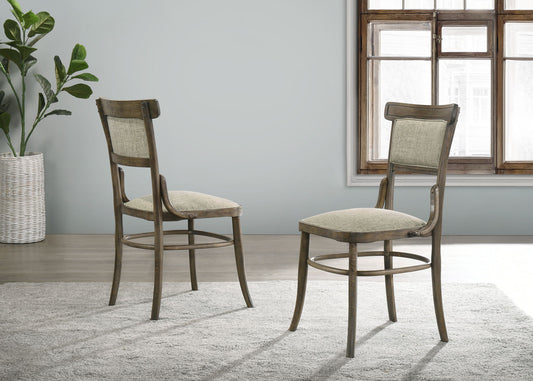 Two Bistro Wide Contemporary Fabric Dining Chairs with cushions in Vintage Walnut are set on a gray rug in a bright room with a potted plant, light walls, and a large window letting in natural light.