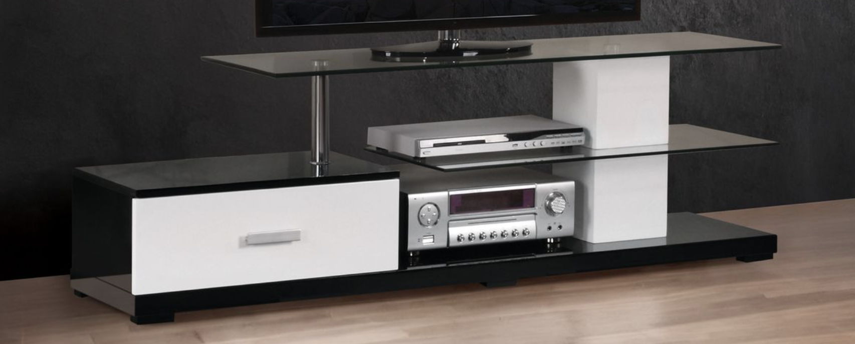 The Ivana TV Stand in white and black features glass shelves for a DVD player and stereo receiver, a left-side drawer, and is set on a wooden floor against a dark wall.
