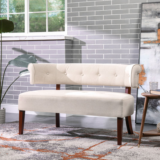 The Jared - Versatile Roll Arm Tufted Bench Settee with a modern beige finish, button-tufted backrest, and wooden legs sits in a bright room with gray brick walls, large window, indoor plants, art, and a round side table on a patterned rug.