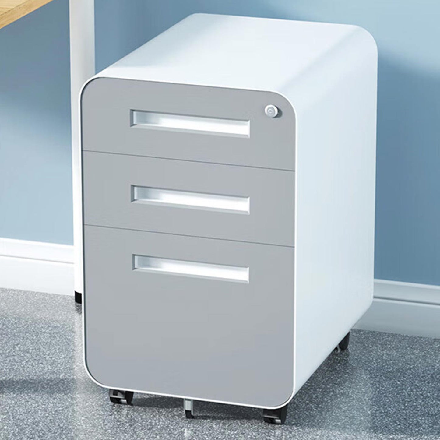 A 3 Drawer Mobile File Cabinet in gray and white cold rolled steel, with lock and 5-wheel anti-tilting design, sits next to a wooden desk on a speckled gray floor, against a blue wall. Suitable for legal/letter/A4 files; waterproof and moisture-proof.