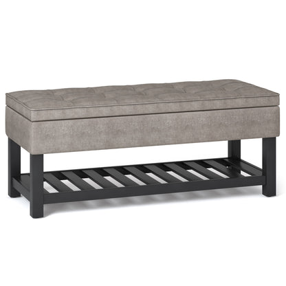 The Cosmopolitan Storage Ottoman Bench features a rectangular gray upholstered seat with a tufted top, black wooden legs, and an open slatted lower shelf.