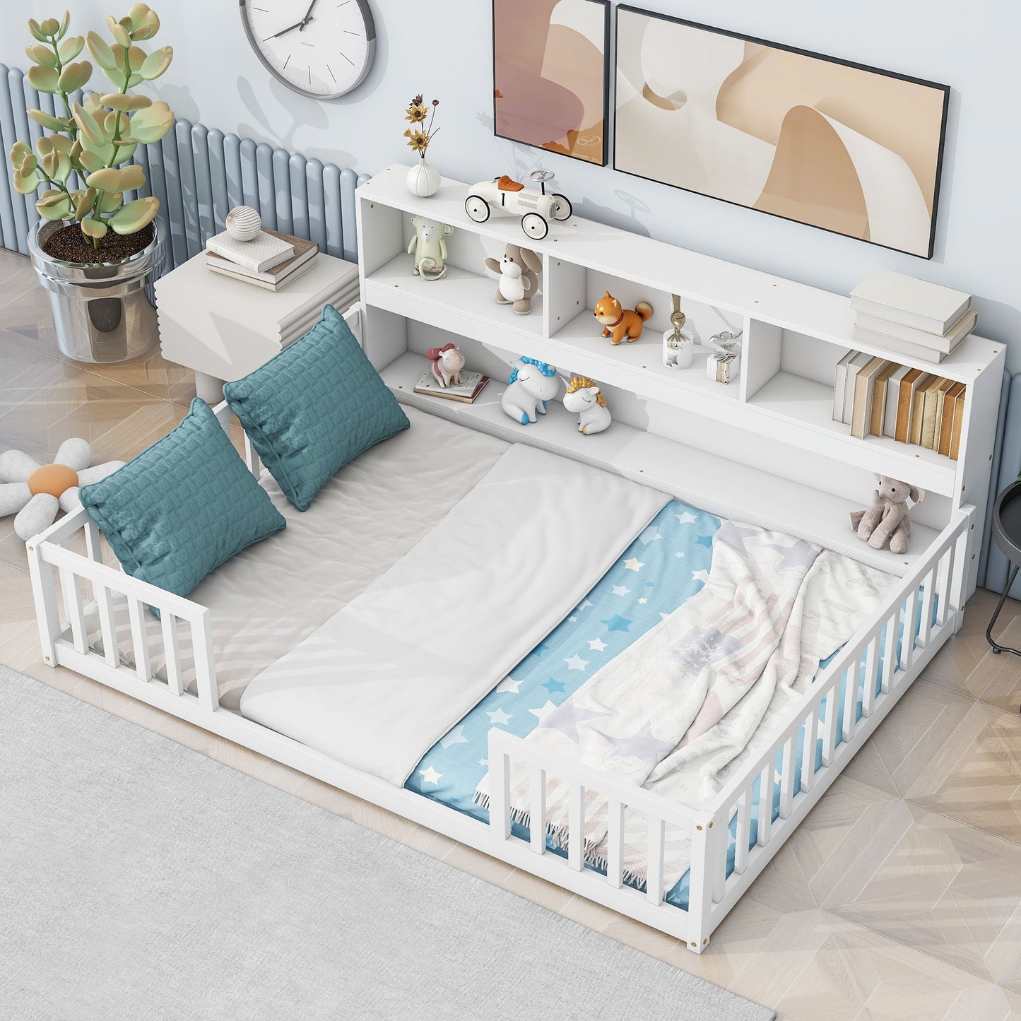 A Floor Bed With Side Bookcase, Shelves, and Guardrails with blue and white bedding and teal pillows sits in a bright room. The headboard's shelves hold stuffed animals and toys; a plant, clock, and abstract art are visible in the background.