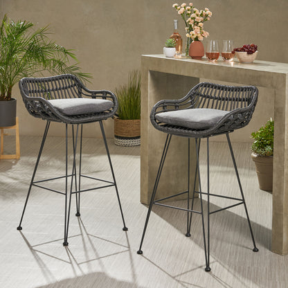 Two Outdoor Rattan Bar Chairs with metal legs and gray cushions sit by a stone bar table topped with potted plants, drinks, glasses, and cherries, creating a stylish modern scene for indoor or patio use.