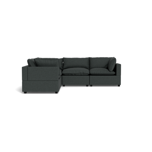 The Kova Pillow Cushion Corner Sectional, an L-shaped sofa in dark gray with cushioned seats and backrests, is shown from the front against a black background.
