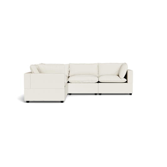 The Kova Pillow Cushion Corner Sectional, an L-shaped sofa with cream upholstery and plush cushions, is shown from the front against a plain black background.