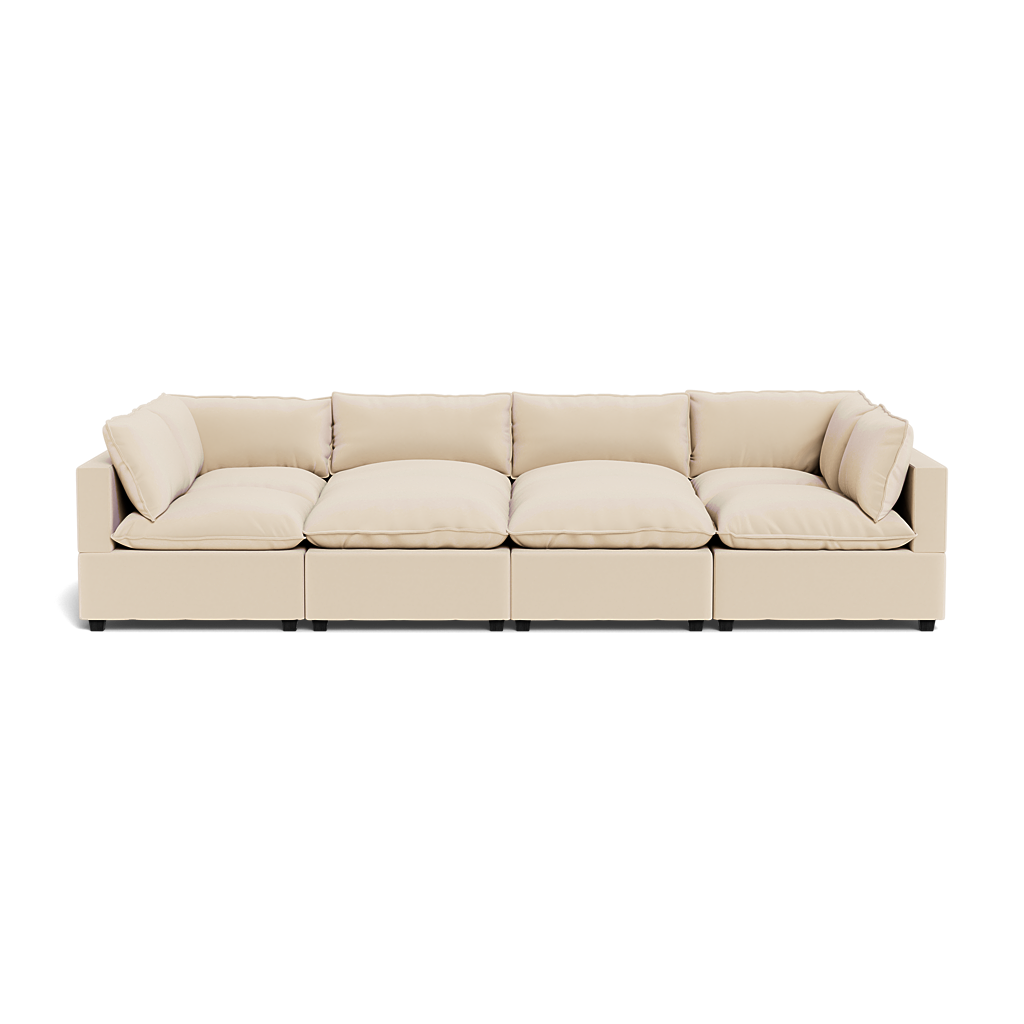 The Kova Pillow Cushion Grand Pit is a modern beige sectional sofa featuring four large seat cushions and multiple matching back and side cushions, shown from the front against a white background.