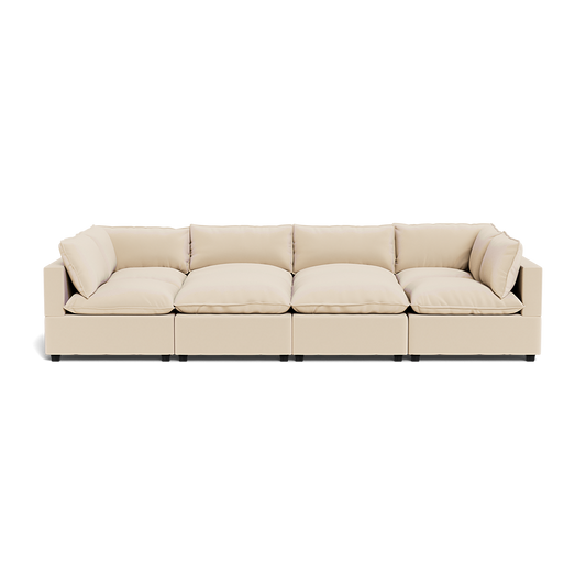 The Kova Pillow Cushion Grand Pit is a modern beige sectional sofa featuring four large seat cushions and multiple matching back and side cushions, shown from the front against a white background.