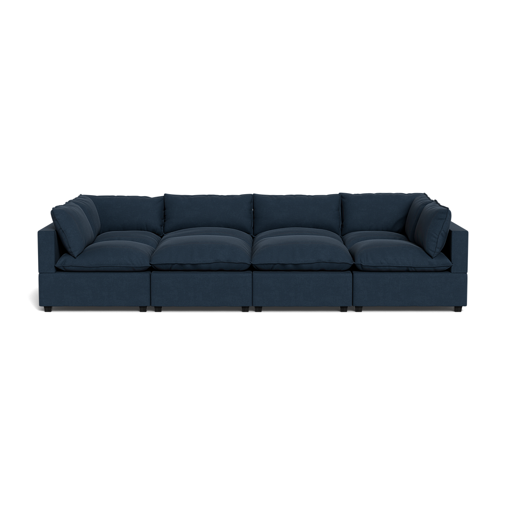 The Kova Pillow Cushion Grand Pit is a large, dark blue sectional sofa with five cushioned seats and matching back and side pillows, shown from the front against a black background.