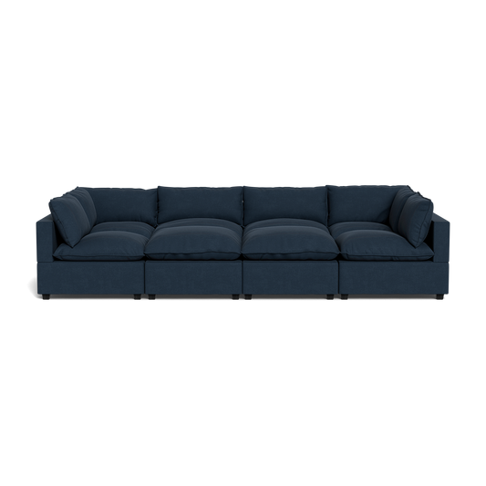 The Kova Pillow Cushion Grand Pit is a large, dark blue sectional sofa with five cushioned seats and matching back and side pillows, shown from the front against a black background.