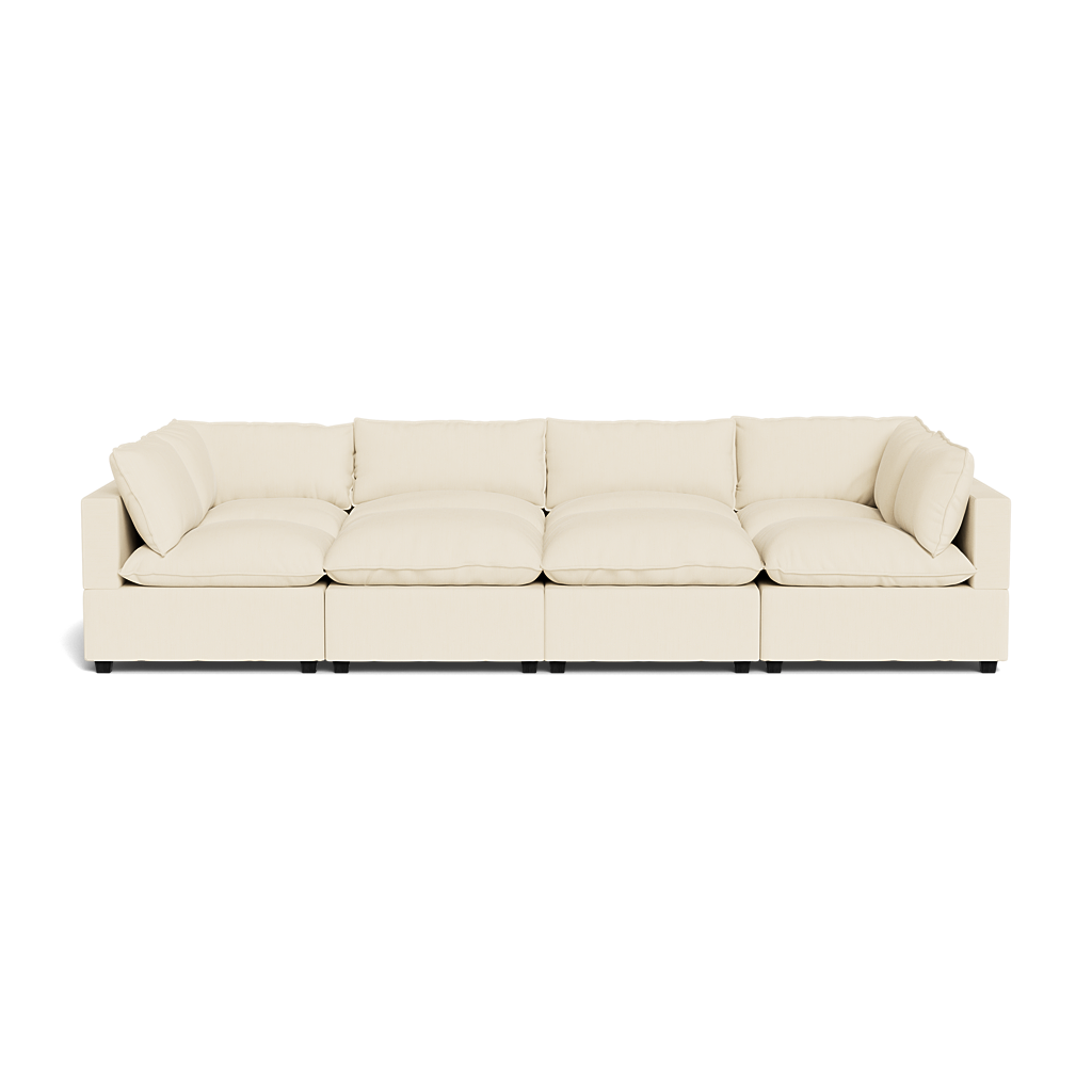 The Kova Pillow Cushion Grand Pit is a modern, long, cream-colored sectional sofa featuring deep cushions and low armrests, shown from the front against a plain white background.