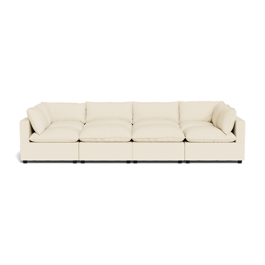 The Kova Pillow Cushion Grand Pit is a modern, long, cream-colored sectional sofa featuring deep cushions and low armrests, shown from the front against a plain white background.