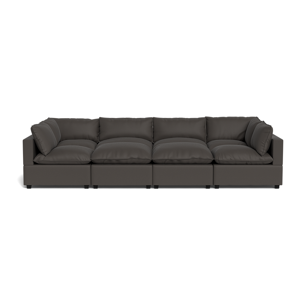 The Kova Pillow Cushion Grand Pit is a modern dark gray sectional sofa with four seat cushions and matching back and side cushions, shown from the front against a plain black background.